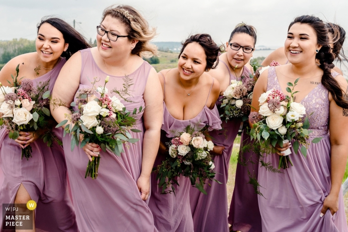 Photo by: <a href="https://www.wpja.com/contests/2019-v12/best-wedding-photographers/2547444">Chrystal Stringer - Edmonton Alberta</a> Fort Chipewyan, Alberta Wedding Day Photography - Bridesmaid watching the bride come down the aisle during outdoor, windy ceremony