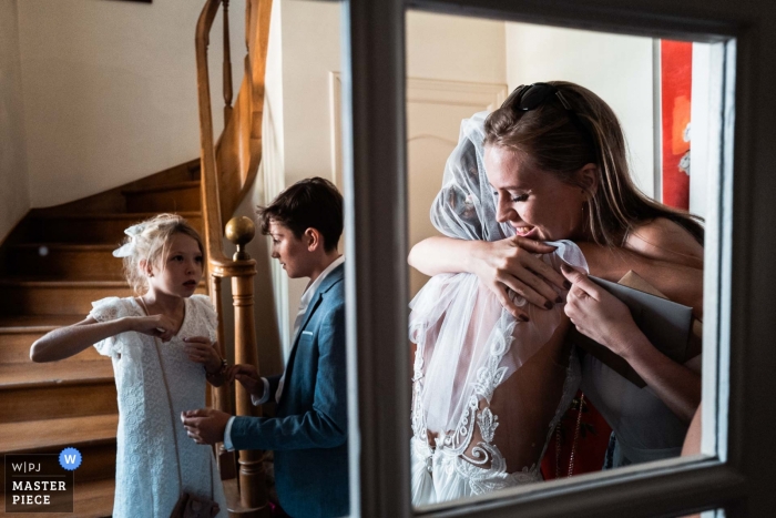 Un amico bacia la sposa con emozione attraverso la finestra il giorno del matrimonio in Francia. | Fotografia di matrimonio in Savoia