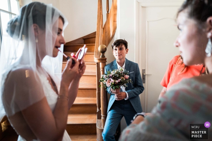 Novia francesa preparándose para su ceremonia mientras el hermano pequeño admira el maquillaje de la novia con atención