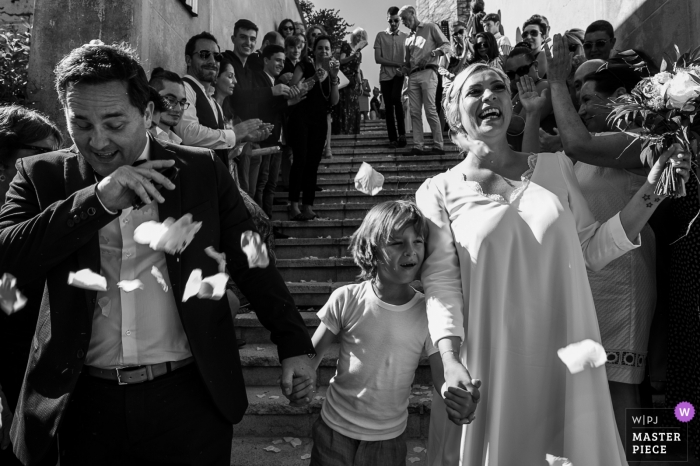 La sposa, lo sposo e il figlio colpiti dai coriandoli dagli ospiti dopo la cerimonia di nozze al castello di Candie, Chambéry, Francia.