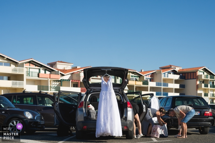 Photo by: <a href="https://www.wpja.com/contests/2019-v12/best-wedding-photographers/2548033">Franck Petit - Serignac sur Garonne </a> Vieux Boucaut, France wedding photo of the bridal party arriving in the parking lot, as weddng dress hangs from the backdoor hatchh of the car.