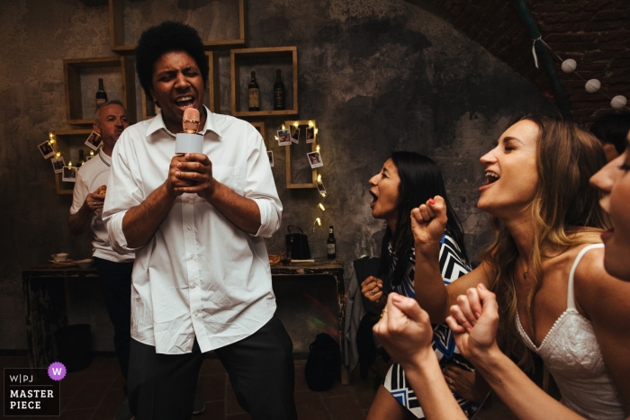 Photo by: <a href="https://www.wpja.com/contests/2019-v12/best-wedding-photographers/2548086">Lyndsey Goddard - London London</a> United Kingdom wedding reception image of the bride and frineds singing with the groom's brother