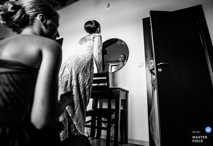 Photo by: <a href="https://www.wpja.com/contests/2019-v12/best-wedding-photographers/2548136">Boni Bonev - Sofia Sofia</a> Pirin Golf Club, Razlog , Bulgaria | Bride looking in mirror as a young bridesmaid peaks into the room out of curiosity.