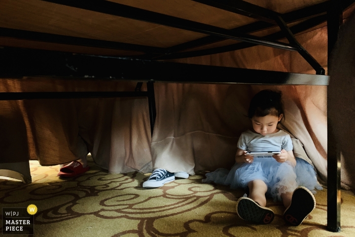 Photo by: <a href="https://www.wpja.com/contests/2019-v12/best-wedding-photographers/2548280">Zhongkun Zhang - Sanming </a> Fujian Hotel room wedding day photography | Children hide under the dining table and play with their mobile phones