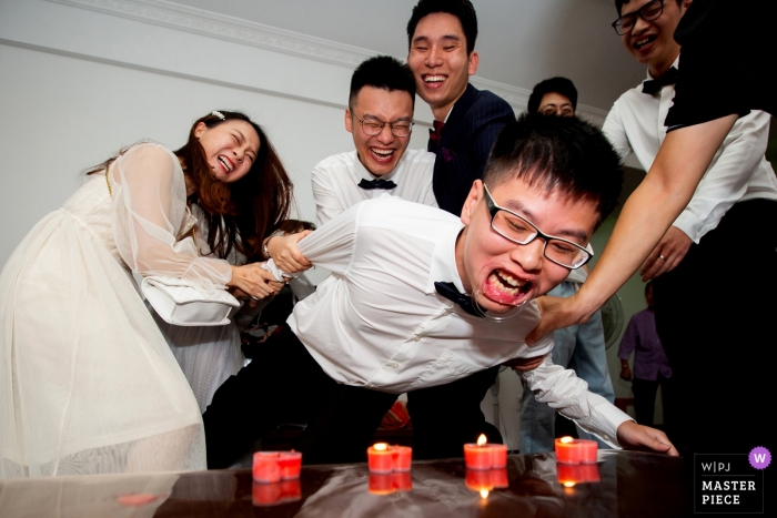 Photo by: <a href="https://www.wpja.com/contests/2019-v12/best-wedding-photographers/2548286">Zhongkun Zhang - Sanming </a> Fujian Groomsman Game trying to blow out candles - China Actual Day Wedding Photographer
