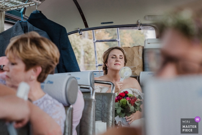 Photo by: <a href="https://www.wpja.com/contests/2019-v12/best-wedding-photographers/2548390">Nadine Lotze - Hagen Nordrhein-Westfalen</a> Schloss Nordkirchen summer wedding photography | The bride is too hot - using small fan in back of bus