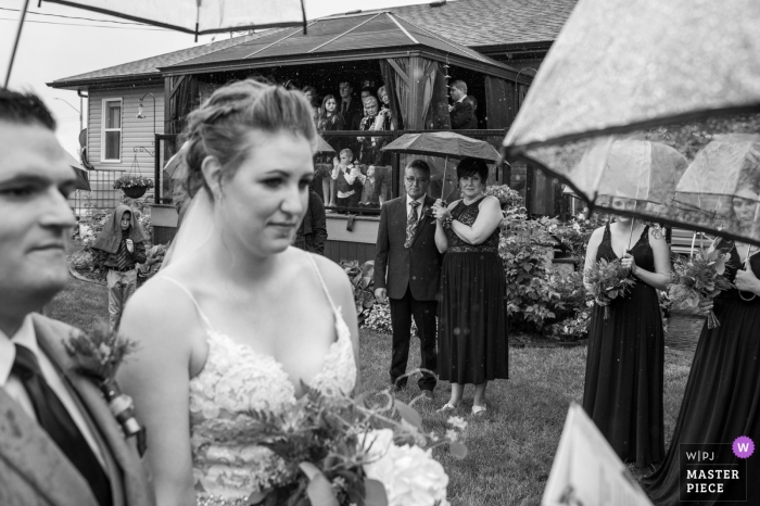 Fotografia do quintal dos pais da noiva, Daysland, AB, Canadá - imagem da cerimônia de casamento tirada durante a chuva sob guarda-chuvas