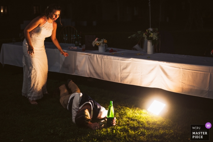 Foto von: <a href="https://www.wpja.com/contests/2019-v12/best-wedding-photographers/2548666"> Dejan Zagar - Teharje </a> Hochzeitsfotografie - Dvorec Rakičan - Slowenien | Braut, die für den Bräutigam kommt, der draußen auf dem Gras mit Flasche liegt