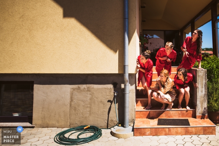 Fotografia de casamento na Eslovênia na casa da noiva - As damas de honra estão verificando o noivo que vem buscar a noiva