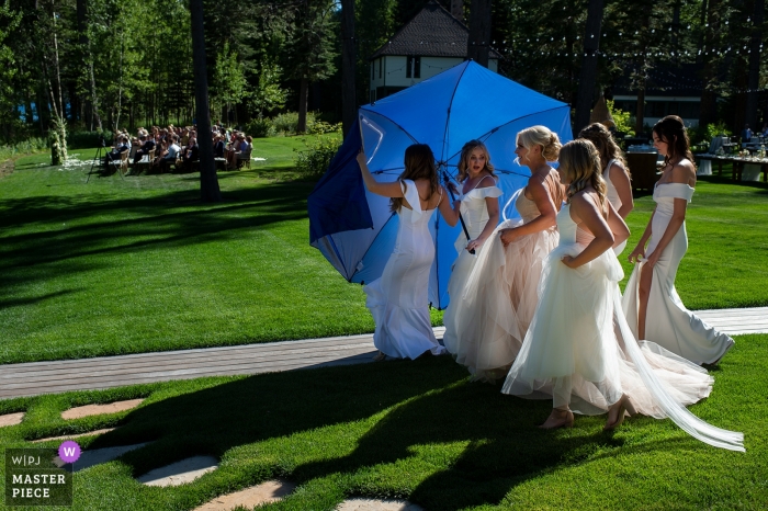 Photo by: <a href="https://www.wpja.com/contests/2019-v12/best-wedding-photographers/2548704">Tara Theilen - Carson City Nevada</a> West Shore Lake Tahoe, CA Wedding Photography - Image of Bridesmaids hide the bride behind an umbrella on the way to her ceremony.