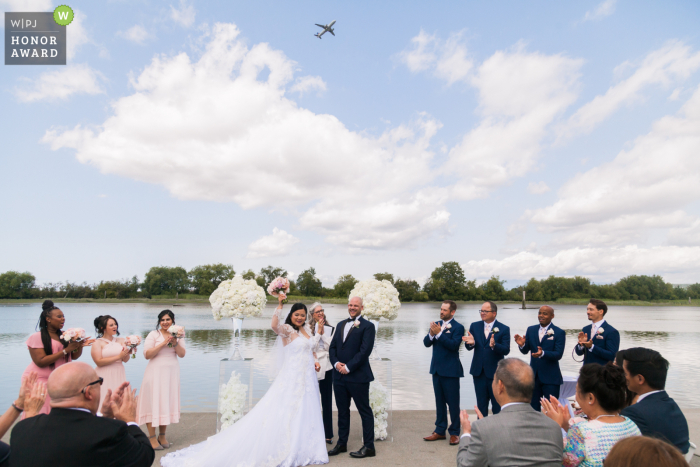 Um avião voa pelos noivos Foto do local do casamento ao ar livre da UBC Boathouse, Richmond, BC | Um avião voa enquanto os noivos comemoram.