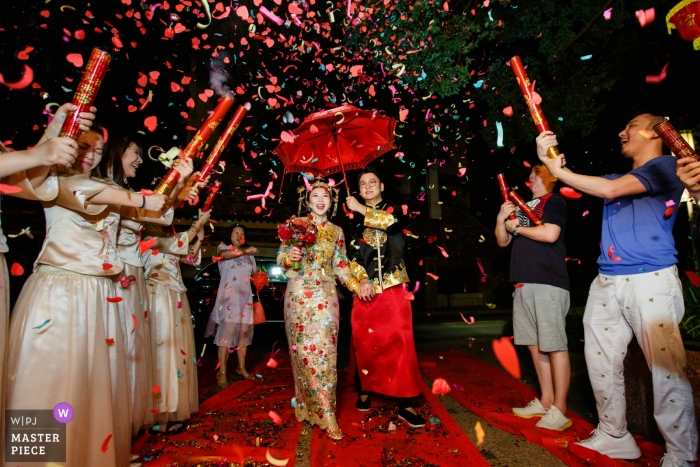 Dongguan, China werkelijke dag bruiloft fotografie van de bruid en bruidegom - terug naar huis onder rode paraplu en confetti kanonnen