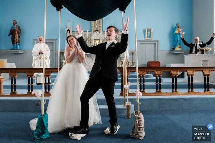 Photo by: <a href="https://www.wpja.com/contests/2019-v13/best-wedding-photographers/2549816">Jonathan Ryder - Belfast County Antrim</a> Wedding Ceremony Photography: St Mary's Church, Ballybrack, Co. Donegal. The groom celebrates as he manages to break the glass during the Jewish part of the ceremony, joined by his father in law and the priest, towards the back.