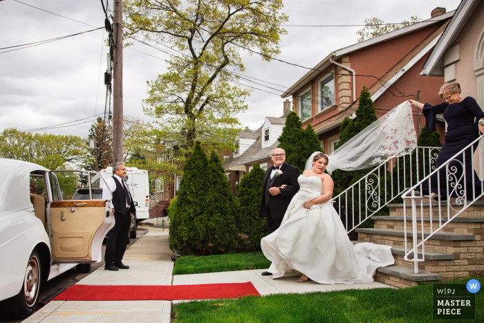 Photo: <a href="https://www.wpja.com/contests/2019-v13/best-wedding-photographers/2550918"> Todd Laffler - Haut pont du New Jersey </a> Photographie de mariage du New Jersey | La mariée est escortée dans une voiture avant la cérémonie, maman tient le voile derrière la mariée trop étroitement, la mariée donne un coup d'oeil