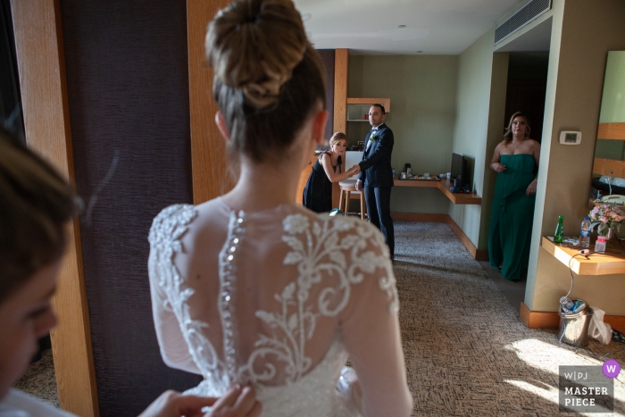 Fotografia di hotel in Turchia il giorno del matrimonio | Lo sposo e gli amici guardano la sposa mentre si mette il vestito