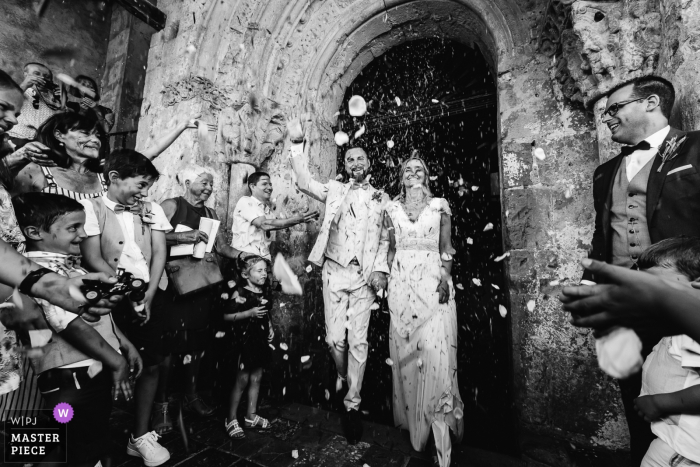 Photo by: <a href="https://www.wpja.com/contests/2019-v14/best-wedding-photographers/2552275">Damien Dohmen - Pau </a> Simacourbe, France wedding photography of the bride and groom exiting the church as their guests greet them.