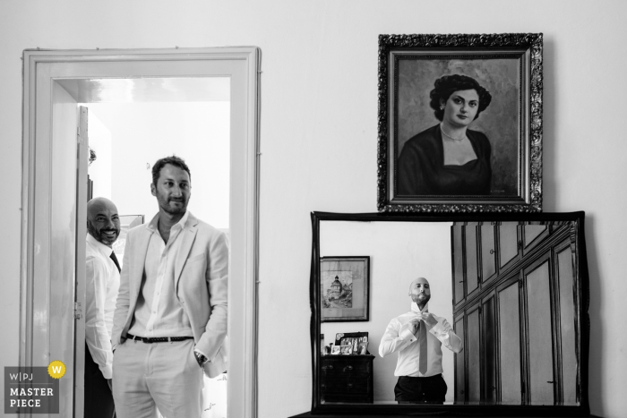 Zdjęcie: <a href="https://www.wpja.com/contests/2019-v14/best-wedding-photographers/2552374"> Nino Lombardo - Taormina Trapani </a> Fotografia ślubna Trapani pana młodego, szykującego się w lustrze, gdy obserwują go przyjaciele.