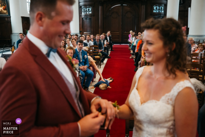 Photo by: <a href="https://www.wpja.com/contests/2019-v14/best-wedding-photographers/2553168">Fille Roelants - Antwerpen Antwerpen</a> Church of Sint-Niklaas - Wedding Photography - As the bride and groom are exchanging rings, the godchild of the groom is having a mental breakdown and decides to lay down in the middle of the isle.