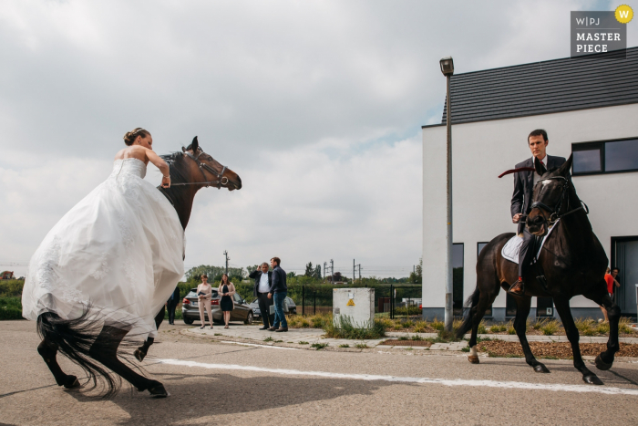 Huwelijksfotografie op straat voor het huis van de Bruidegom en de bruid | Bruid en bruidegom maken zich klaar om te paard naar het stadhuis te gaan en proberen hun paarden te troosten.