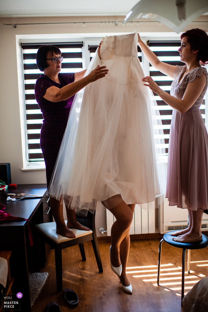 Photo by: <a href="https://www.wpja.com/contests/2019-v14/best-wedding-photographers/2553335">Bozhidar Krastev - Ruse </a> Sofia, Bulgaria wedding photograph of the bride hidden beneath her dress as she gets help.