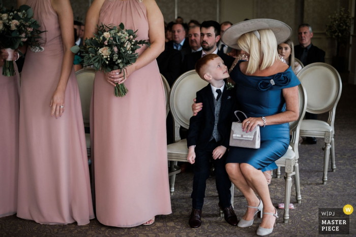 Fotografia de reportagem de casamento do local: Corick House Hotel, Irlanda do Norte | O pajem recebe um abraço de sua avó após entregar com sucesso os anéis de seus pais ao oficiante