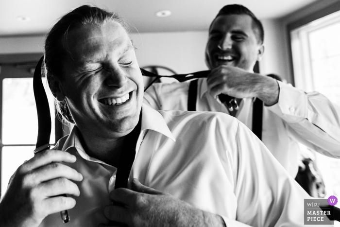 Foto por: <a href="https://www.wpja.com/contests/2019-v14/best-wedding-photographers/2553614"> Michelle Arlotta - Milford New Jersey </a> Padrino de boda ayuda a otro padrino de boda a ponerse sus tirantes en la boda de Bear Brook Valley, NJ - Fotoperiodismo de bodas en Nueva Jersey