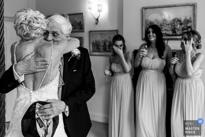 Photo by: <a href="https://www.wpja.com/contests/2019-v14/best-wedding-photographers/2554064">Andy Griffiths - St. Helens Lancashire</a> Iscoyd Park Wedding Reportage Photography - Dad hugging bride with bridesmaids in the back crying