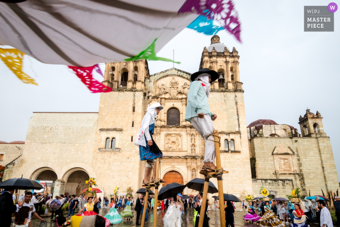 Bride and groom celebrate with the sancudos, mosquitos, stilt-walkers of the calenda after leaving the church Santo Domingo Church, Centro Histórico, Oaxaca, Mexico Wedding Photography - Bride and groom celebrate with the "sancudos" ("mosquitos"; stilt-walkers) of the calenda after leaving the church