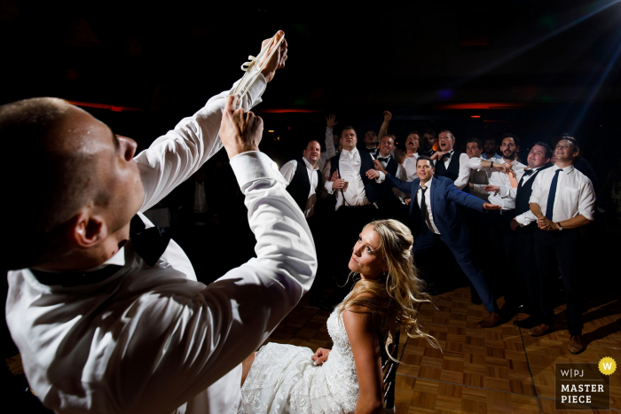 The Broadmoor Hotel, Colorado Springs, Colorado Wedding Venue Photographer -Lo sposo si prepara a girare la giarrettiera mentre i single si spingono per la posizione sulla pista da ballo durante un ricevimento di nozze al Broadmoor.