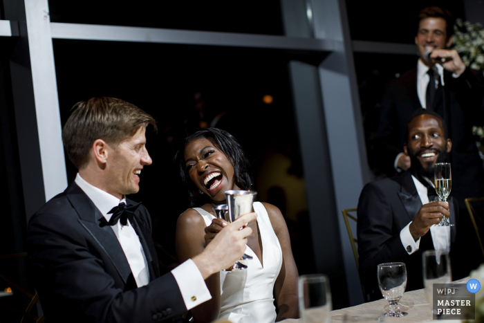 Photo by: <a href="https://www.wpja.com/contests/2019-v14/best-wedding-photographers/2554365">Justin Edmonds - Denver Colorado</a> The bride and groom share a laugh during a toast at the Denver Museum of Nature and Science - Colorado Wedding Photographer