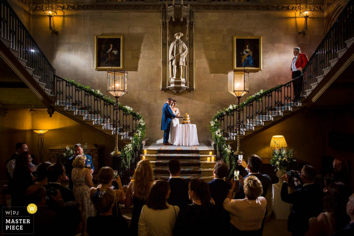 Photo by: <a href="https://www.wpja.com/contests/2019-v15/best-wedding-photographers/2555030">Aaron Storry - Kettering Northamptonshire</a> Ashridge House, United Kingdom Wedding Photographer — Cutting the Cake on the stairs with guests watching