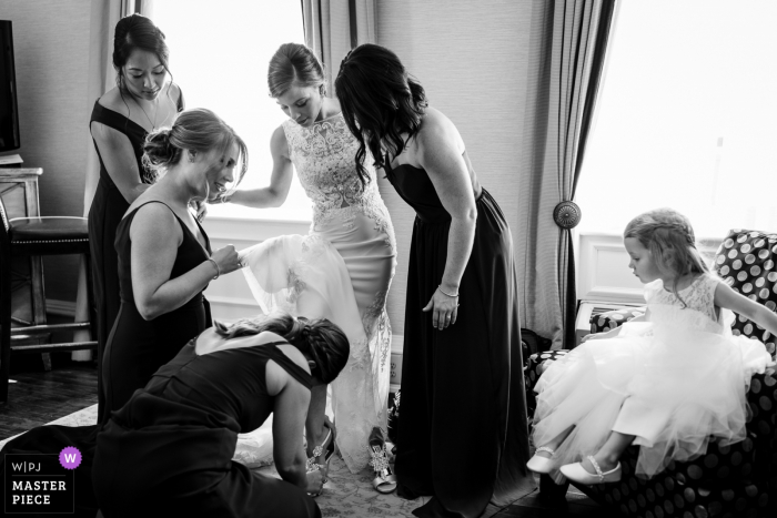 Fotografia di hotel il giorno del matrimonio - Le damigelle aiutano la sposa a mettersi le scarpe mentre la fioraia guarda