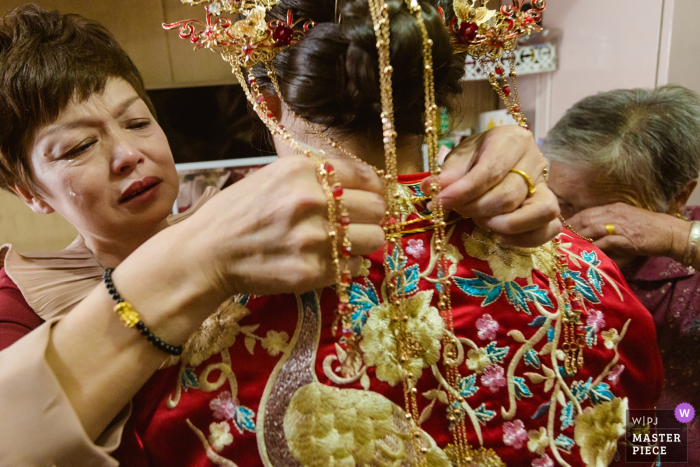 Fotografia di matrimonio nel Fujian della madre della sposa che aiuta la sposa a prepararsi mentre è in lacrime prima della cerimonia di matrimonio.