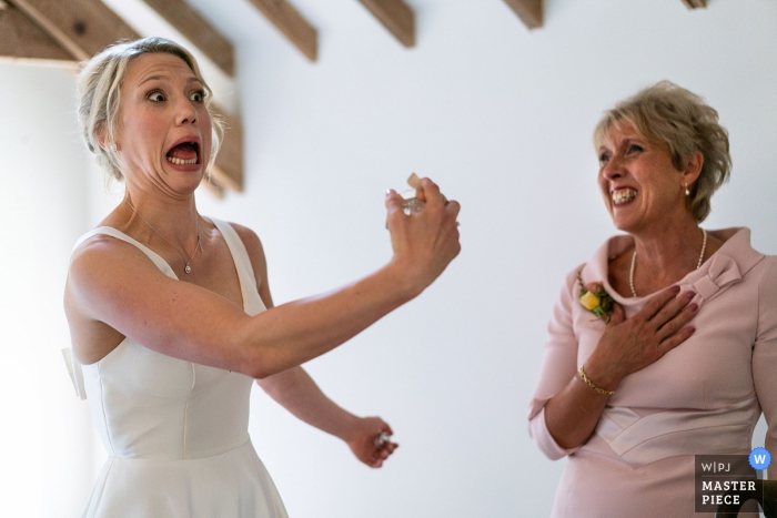 Hochzeitsfotografie auf der Warborne Farm, New Forest, Hampshire - Braut Laura zieht ein Gesicht, während sie vor ihrer Mutter den letzten Schliff des Parfums aufträgt.