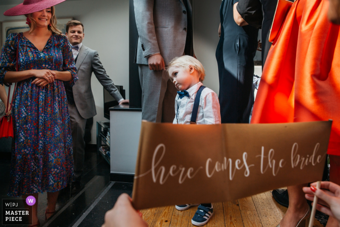 Fotografo di matrimoni delle Fiandre - a casa dei genitori della sposa poco prima della cerimonia Al bambino è stato ordinato di tenere uno striscione "ecco che arriva la sposa" in chiesa, ma non se la sentiva