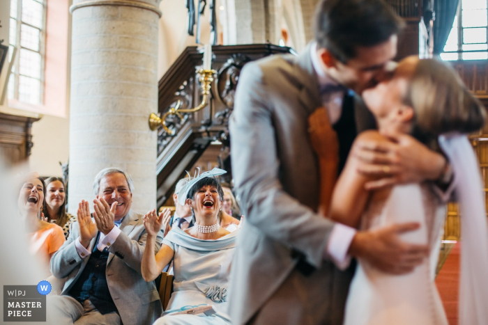 Hochzeitsfotograf der Flandern-Kirche - das Paar küsst sich direkt nachdem der Priester erklärt hat "das Paar kann so lügen, wie die Leute applaudieren"