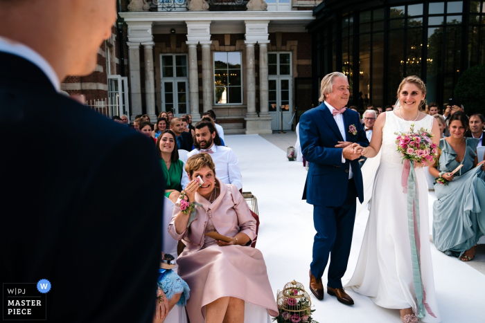 Fotógrafo de la ceremonia de boda al aire libre de Flandes - El padre de la novia trata de regalar a su hija mientras su madre derrama una lágrima de alegría, la novia se ve llena de emoción para el novio