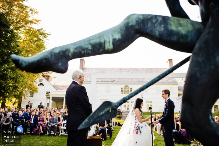 Wedding photography from the Southern Vermont Arts Center — The bride and groom are framed by a sculpture during their ceremony