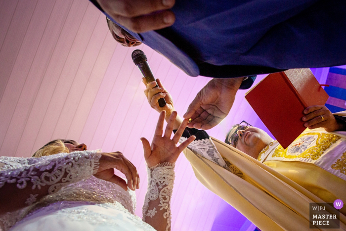 Photo by: <a href="https://www.wpja.com/contests/2019-v15/best-wedding-photographers/2557510">Claudia Amorim - Goiânia Goias</a> Paróquia São Paulo Apóstolo low angle wedding ceremony photograph of the groom putting the ring on the finger of the bride