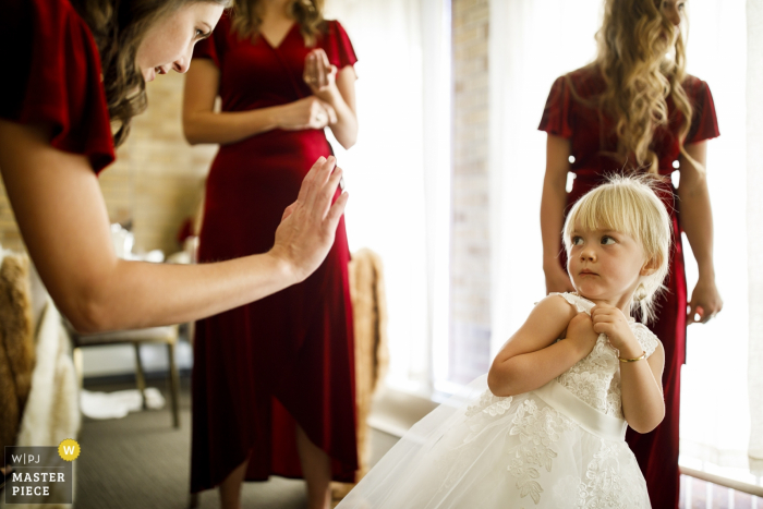 Foto von: <a href="https://www.wpja.com/contests/2019-v15/best-wedding-photographers/2557529"> Justin Edmonds - Denver Colorado </a> Katholische Kirche Unserer Lieben Frau von Lourdes, Denver, CO Hochzeitsfotograf - Das Blumenmädchen reagiert, wenn eine Brautjungfer sie auffordert, ein High Five zu machen, während sie sich auf die Hochzeit vorbereitet.