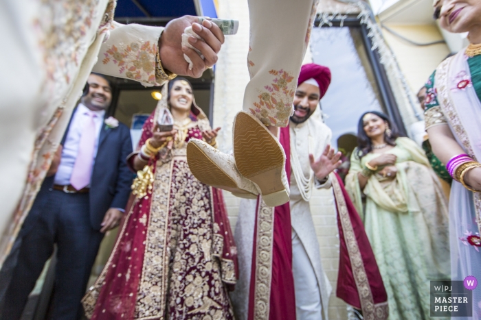 Foto: <a href="https://www.wpja.com/contests/2019-v16/best-wedding-photographers/2560751"> Andrew Morrell - Winchester Virginia </a> Sikh Association of Baltimore, Randallstown, MD Hochzeitsfotograf - Holt sich Schuhe, während der Tender nach einer zügigen Verhandlung nach der Zeremonie die Hände austauscht.