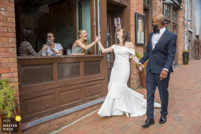 Photo by: <a href="https://www.wpja.com/contests/2019-v16/best-wedding-photographers/2561280">Simon Cardwell - London London</a> Asheville, North Carolina High Five for the bride as she walks down the street with her groom - Wedding Day Photography