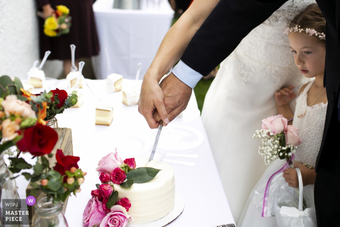 Foto door: <a href="https://www.wpja.com/contests/2019-v16/best-wedding-photographers/2561759"> Heather DeCamp - Chicago Illinois </a> De fotograaf van de de binnenplaatshuwelijk van Los Angeles Californië - Beeld van een bloemenmeisje die binnen tijdens het cakeknipsel gluren