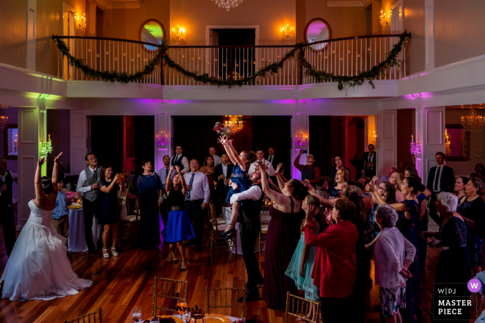 Photo by: <a href="https://www.wpja.com/contests/2019-v16/best-wedding-photographers/2562383">Brittany Diliberto - Arlington Virginia</a> Rose Hill Manor, Raspberry Plain, Leesburg VA Wedding Photographer | The flower girl is lifted into the air as the bride throws the bouquet. Wedding photography from the reception venue.