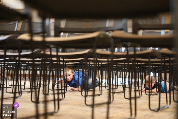 Photo by: <a href="https://www.wpja.com/contests/2019-v16/best-wedding-photographers/2562408">Abby Paul - Fargo North Dakota</a> Children climb under the chairs at a Fargo North Dakota - Wedding Photojournalism
