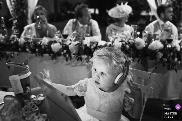 Photo by: <a href="https://www.wpja.com/contests/2019-v17/best-wedding-photographers/2563294">Franck Boutonnet - Lyon </a> Abbaye de Taloire France wedding photography - a little girl watch her tablet during the speeches