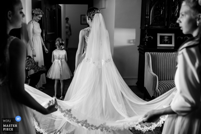 Photo by: <a href="https://www.wpja.com/contests/2019-v17/best-wedding-photographers/2563464">Matouš Bárta - Prague </a> Chateau Valeč wedding image of bride preparing to exit her room to the ceremony as her attendants hold her long veil.