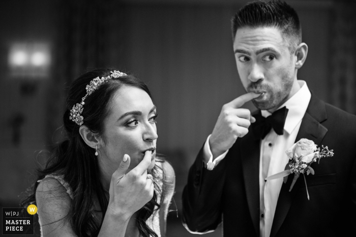 Photo by: <a href="https://www.wpja.com/contests/2019-v17/best-wedding-photographers/2563978">Michelle Arlotta - Milford New Jersey</a> Bride and groom simultaneously lick cake off their fingers while making surprised reactions at Edgewood Country Club NJ wedding
