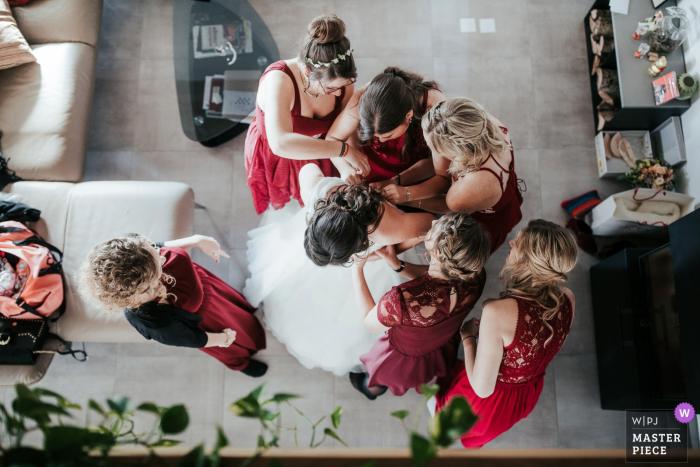 Photo by: <a href="https://www.wpja.com/contests/2019-v17/best-wedding-photographers/2564346">Vincent Bourrut - La Neuveville Bern</a> Onnen, Switzerland wedding photography showing the bride Getting ready in this overhead image with bridesmaids in red dresses