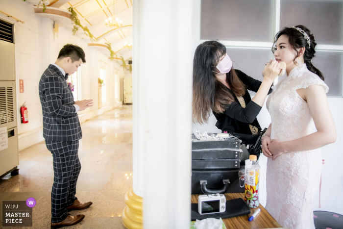 Photo by: <a href="https://www.wpja.com/contests/2019-v17/best-wedding-photographers/2564923">Ke-Wan Li - TaiChung City </a> Wedding Photography, Taiwan. Bride getting makeup with groom waiting.